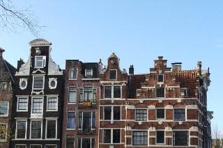 A picturesque row of historic Dutch canal houses with intricate gables and large windows under a clear blue sky evokes a serene European cityscape ideal for cultural exploration and photography.
