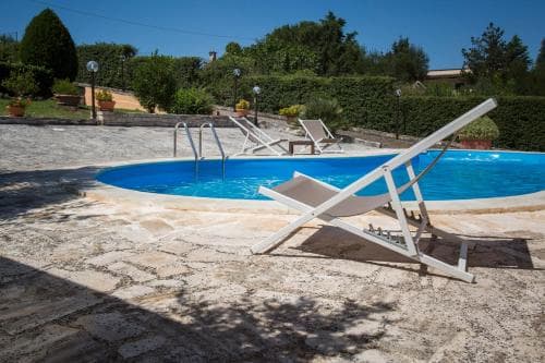 A serene outdoor poolside scene with lounge chairs on a stone patio, surrounded by lush greenery, ideal for relaxing summer vacations.