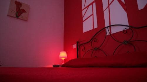 A cozy bedroom bathed in red hues features a decorative wrought iron bed frame, a small lamp casting warm light, and abstract wall art, ideal for travelers seeking a romantic and intimate getaway.