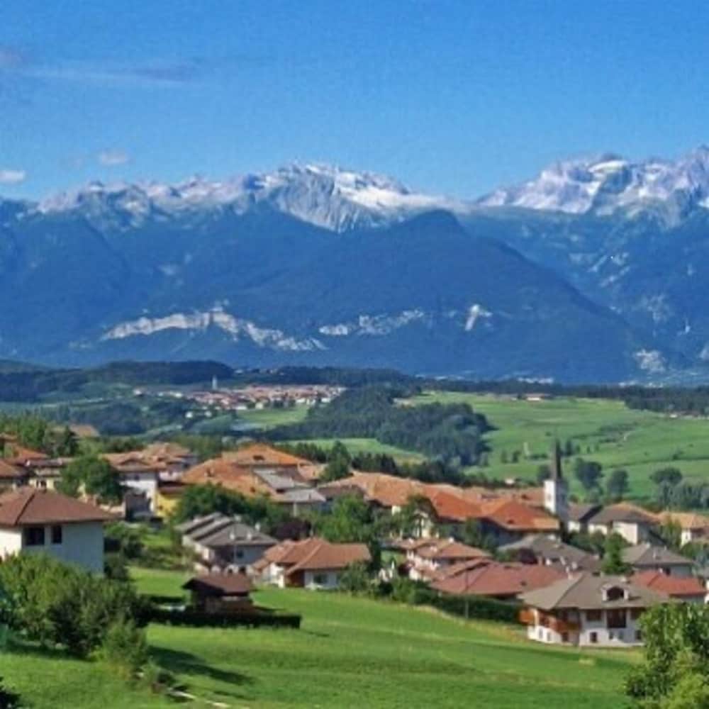 A serene village with red-roofed houses nestled in lush green fields under the majestic backdrop of snow-capped mountains, ideal for tranquil countryside retreats and scenic photography.
