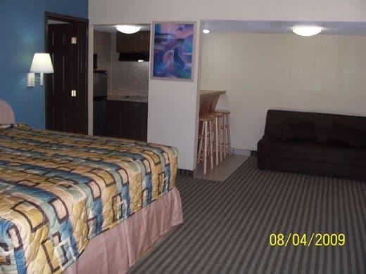 A cozy motel room features a neatly made bed with a colorful quilt, a small kitchenette, a couch, and bar stools, creating a welcoming atmosphere ideal for travelers seeking comfort and convenience.