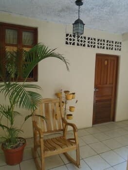 A cozy indoor patio features a wooden rocking chair beside a potted palm plant, under a decorative tiled ceiling, evoking a serene tropical retreat ideal for relaxation and leisure photography.