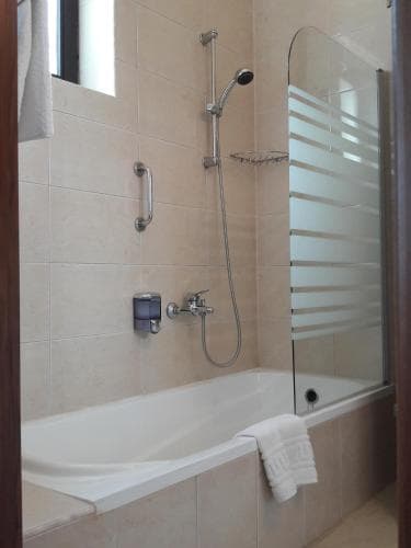 A cozy hotel bathroom features a tiled shower area with a bathtub, modern fixtures, and a frosted glass door, ideal for travelers seeking comfort and cleanliness during their stay.