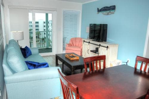 A cozy beachside apartment features a vibrant blue and pink interior with a balcony view, ideal for a relaxing seaside getaway.