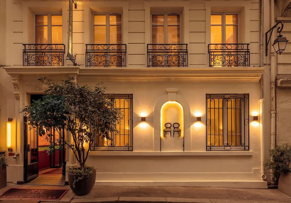 A warmly lit boutique hotel entrance with ornate balconies and inviting outdoor seating creates an elegant evening ambiance perfect for travelers seeking a cozy urban retreat.