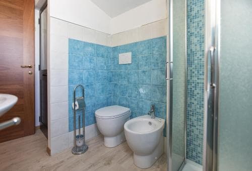 A cozy bathroom with blue-tiled walls, a bidet, toilet, and glass-enclosed shower exudes cleanliness and comfort, ideal for travelers seeking a well-maintained accommodation.