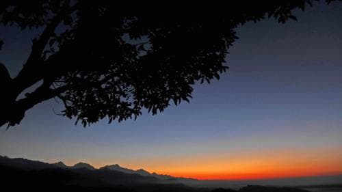 A serene sunset over distant mountains framed by silhouetted tree branches creates a tranquil natural landscape ideal for relaxation and photography.