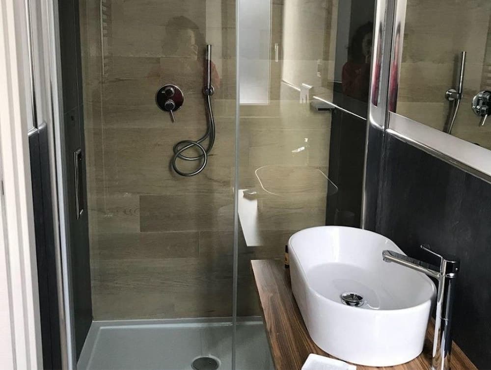 A modern bathroom features a sleek walk-in shower with glass doors, a minimalist sink, and a wooden countertop, creating a clean and contemporary atmosphere ideal for travelers seeking comfort and style in their accommodations.