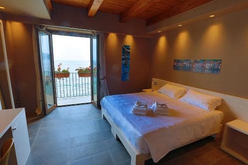 A cozy hotel room with a serene ocean view through an open balcony door, featuring modern furnishings, warm lighting, and vibrant wall art, ideal for travelers seeking relaxation by the sea.