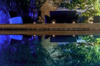 A serene outdoor dining area with modern chairs and string lights reflecting in a tranquil water feature, ideal for romantic evenings or intimate gatherings.