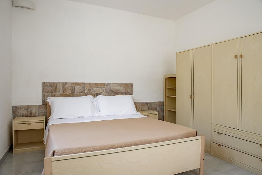 A cozy hotel bedroom features a neatly made bed with a tiled headboard, light wooden furniture, and a minimalist design, ideal for travelers seeking comfort and simplicity.