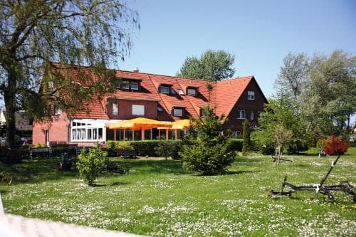 A serene countryside inn with a red-tiled roof, surrounded by lush greenery and vibrant orange umbrellas, offers a peaceful retreat ideal for nature lovers seeking relaxation.