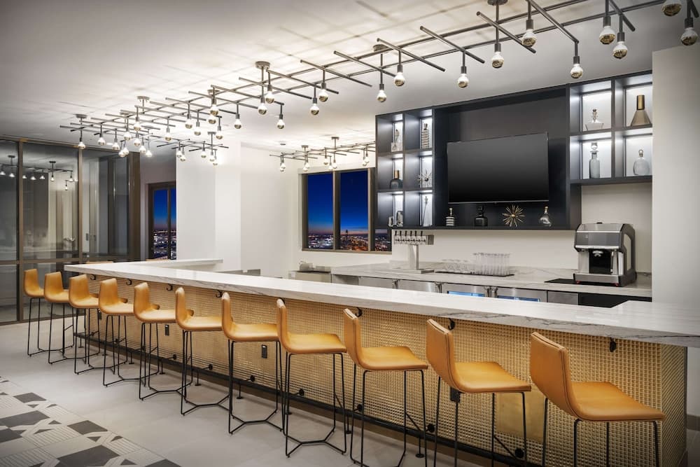 A modern bar area with sleek lighting, orange stools, and a cityscape view through large windows offers an upscale ambiance ideal for evening gatherings or business retreats.