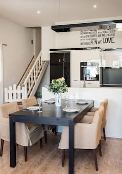 A cozy modern dining area with a sleek black table, beige chairs, and a staircase in the background creates an inviting atmosphere perfect for family gatherings or intimate dinners at home.