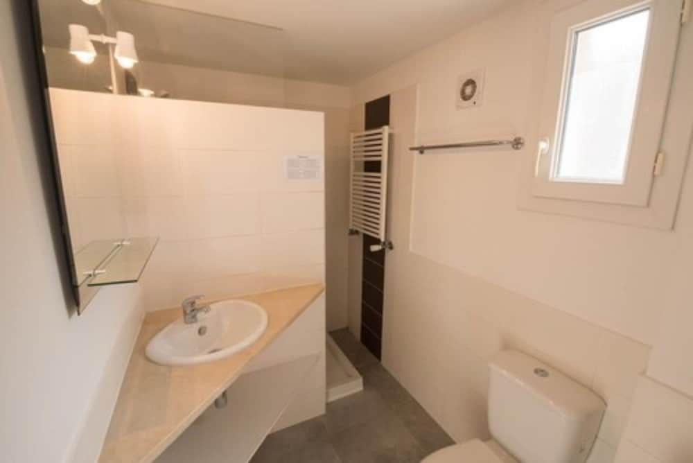 A clean, modern bathroom with white walls, a wooden countertop sink, a towel radiator, and a small window creates a bright and functional space ideal for travelers seeking comfort in accommodations.