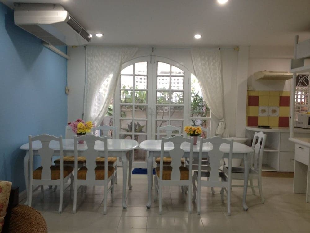 A cozy dining area with white tables and chairs adorned with floral arrangements, set against a backdrop of a bright arched window and colorful kitchen tiles, creates an inviting atmosphere perfect for family gatherings or intimate dinners.