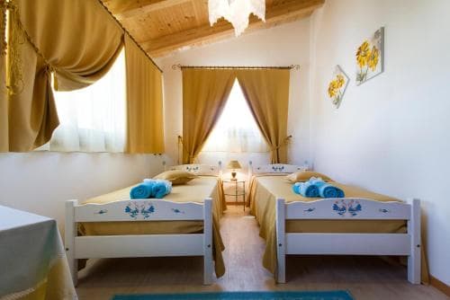 A cozy, sunlit bedroom with twin beds adorned in blue linens, golden curtains, and floral artwork creates a warm and inviting atmosphere ideal for family vacations or retreats.
