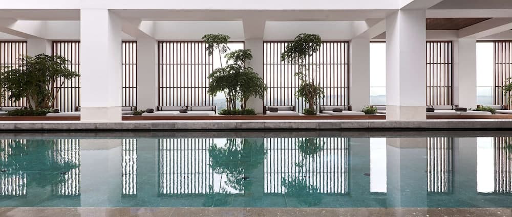 A serene indoor pool area with minimalist architecture, lush greenery, and reflective water creates a tranquil atmosphere ideal for relaxation and wellness retreats.