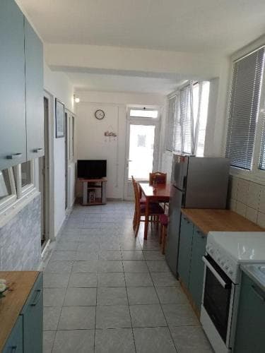 A cozy kitchen-dining area with light blue cabinets, tiled floors, and natural light from windows creates a welcoming atmosphere ideal for travelers seeking a homey rental space.