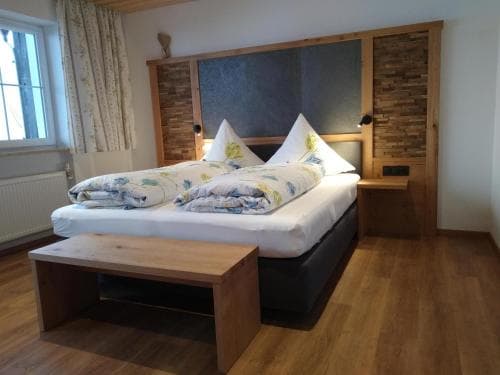 A cozy hotel room with wooden furnishings, a neatly made bed adorned with floral bedding, and soft natural light filtering through the window, ideal for travelers seeking comfort and relaxation.