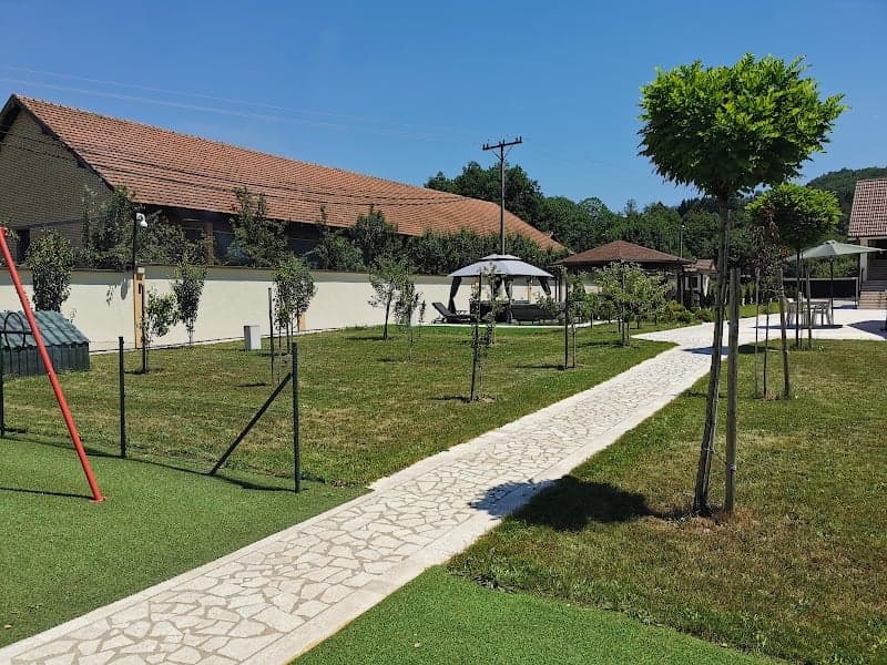 A serene villa retreat in Bosnia and Herzegovina features a well-manicured lawn, stone pathways, shaded seating areas, and a children's play area, ideal for family vacations seeking relaxation and outdoor activities.