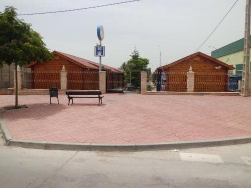 A serene village square features wooden kiosks, benches, and a tiled pavement under an overcast sky, ideal for travelers seeking a quiet rest stop or cultural exploration.