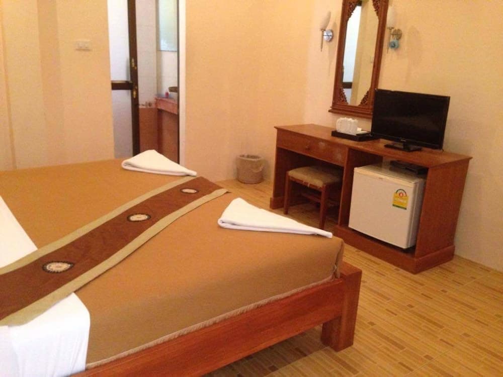 A cozy hotel room features a neatly made bed with decorative linens, a wooden desk with a TV and mini-fridge, and warm lighting, ideal for travelers seeking comfort and convenience.
