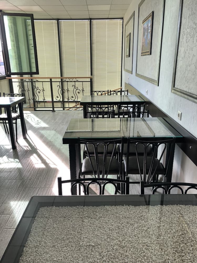 A serene indoor dining area with glass tables, black chairs, and a decorative stone-filled centerpiece, bathed in natural light from large windows with blinds, ideal for a quiet business meeting or casual lunch spot.