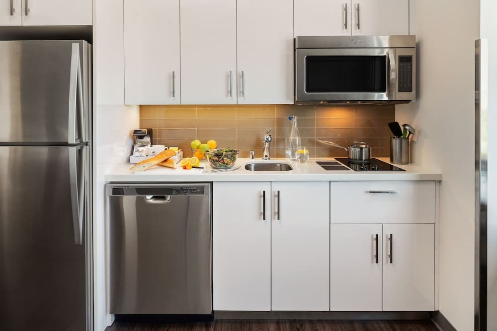 A modern kitchen with sleek white cabinets, stainless steel appliances, and fresh produce on the counter offers a clean and inviting space ideal for travelers seeking a cozy self-catering accommodation.
