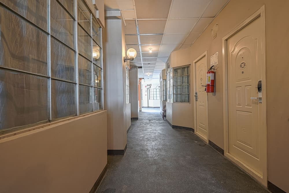 A quiet, utilitarian hotel corridor features frosted glass windows, white doors, and a red fire extinguisher, ideal for travelers seeking a straightforward accommodation experience.