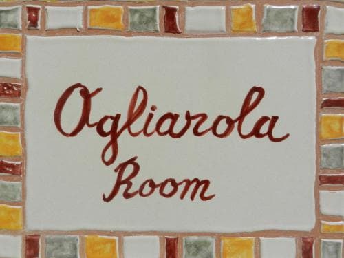 A charming mosaic-framed sign reading "Ogliarola Room" evokes a cozy, rustic ambiance ideal for travelers seeking a unique and personalized accommodation experience.