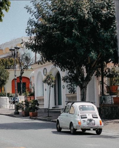 A charming vintage car parked on a quiet street lined with white arches and lush greenery evokes a serene Mediterranean village vibe, perfect for travelers seeking picturesque and tranquil destinations.