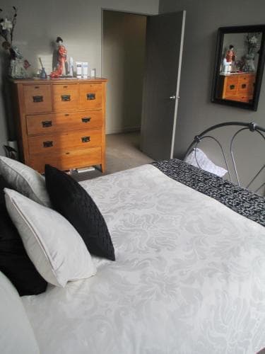 A cozy bedroom with a neatly made bed, wooden dresser adorned with decorative items, and framed artwork creates a serene atmosphere, ideal for travelers seeking a comfortable and stylish accommodation.