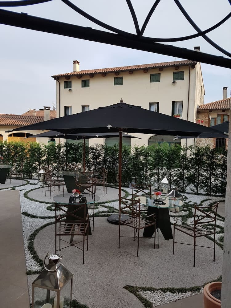 A serene courtyard with geometric gravel patterns, black umbrellas, and metal chairs invites travelers to relax in a quaint European setting, perfect for leisurely dining or quiet contemplation.
