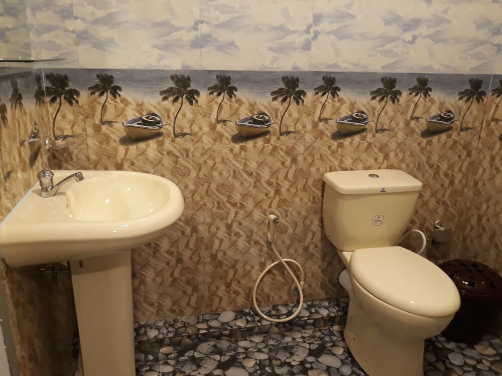 A cozy bathroom features a tropical beach mural with palm trees and boats, paired with a white sink and toilet, creating a serene vacation vibe ideal for travelers seeking relaxation.