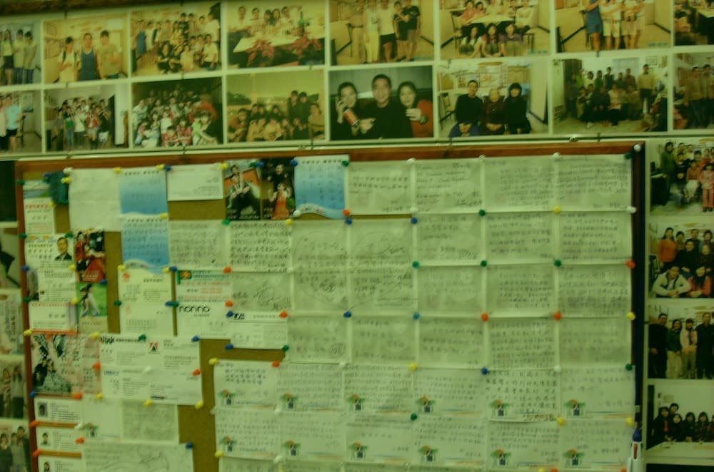 A vibrant community bulletin board filled with handwritten notes and group photos exudes a warm, nostalgic atmosphere, ideal for travelers seeking local insights and connections.