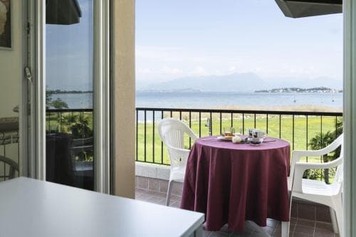A serene balcony with a red tablecloth-covered table overlooks a tranquil coastal landscape, perfect for a relaxing seaside getaway.