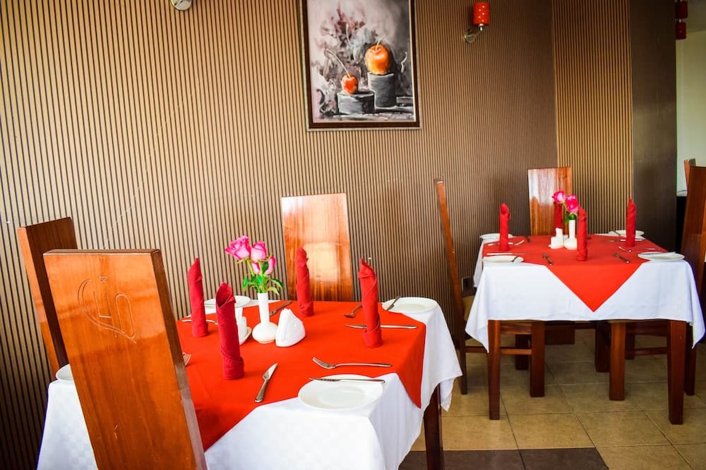 A cozy restaurant interior features warmly lit tables adorned with red napkins and pink roses, creating an inviting atmosphere perfect for romantic dinners or intimate gatherings.