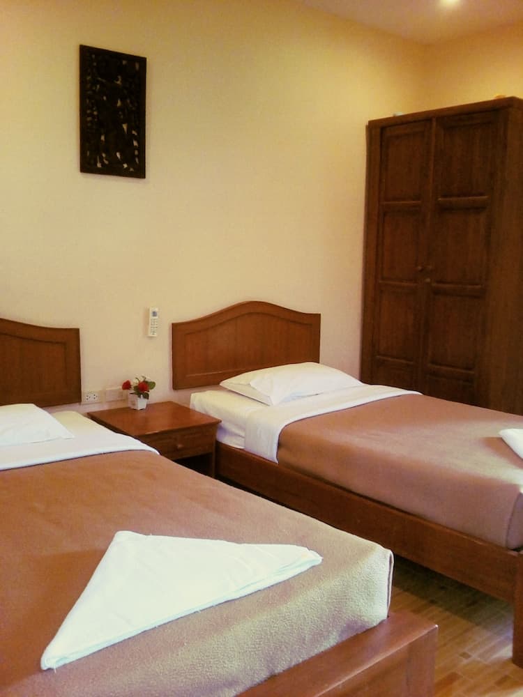 A cozy hotel room features two neatly made wooden beds with white towels folded on top, a wooden wardrobe, and a small table with flowers, ideal for travelers seeking comfort and simplicity.