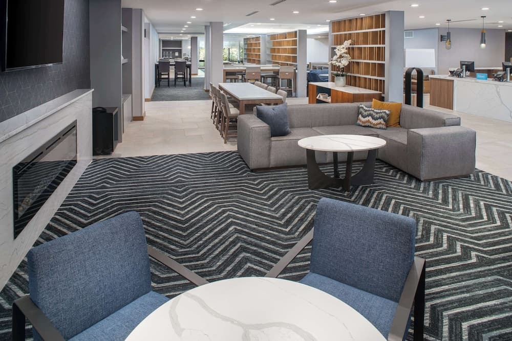A cozy hotel lounge features modern seating, a sleek fireplace, and a zigzag-patterned carpet, creating a welcoming atmosphere ideal for travelers seeking relaxation or business meetings.