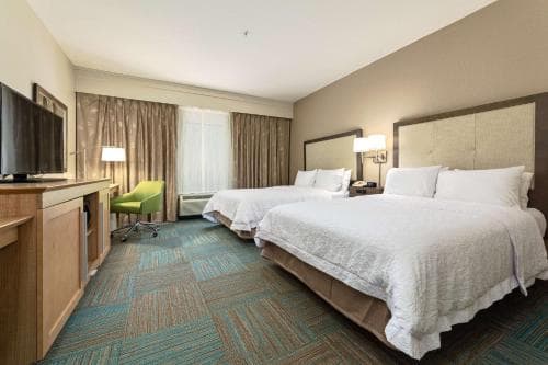 A cozy hotel room features two neatly made beds, a vibrant green chair, and a patterned carpet, creating a welcoming atmosphere ideal for travelers seeking comfort and relaxation.