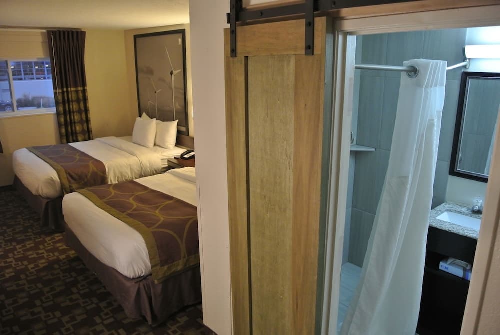A cozy hotel room with two neatly made beds, patterned carpeting, and a rustic sliding barn door leading to a bathroom, ideal for travelers seeking comfort and convenience.