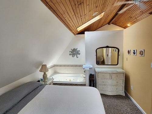 A cozy attic bedroom with a slanted wooden ceiling, a built-in bathtub, and a charming dresser, perfect for a romantic getaway in a boutique hotel.