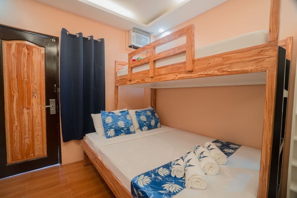 A cozy hostel room with wooden bunk beds adorned with blue floral bedding, neatly rolled towels, and warm peach walls, ideal for budget travelers seeking comfort and simplicity.