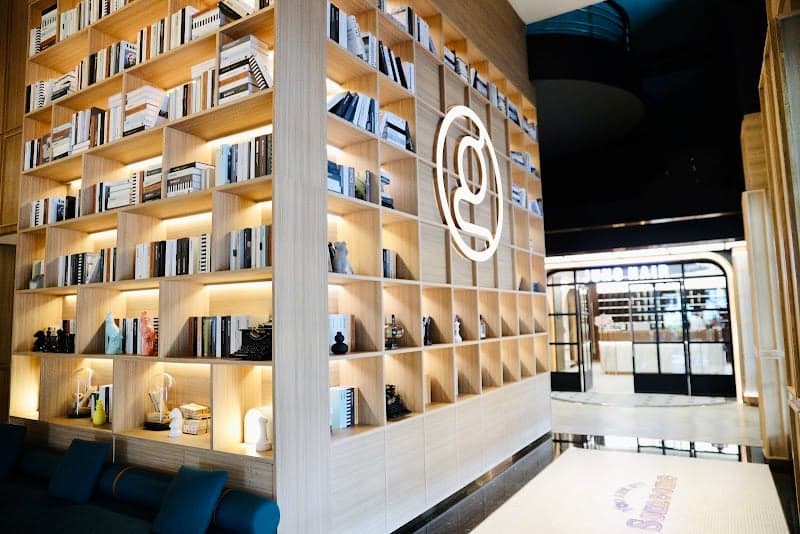 A cozy hotel lobby in Bangkok features a modern wooden bookshelf wall adorned with books and decorative items, creating an inviting atmosphere ideal for travelers seeking a blend of comfort and style.