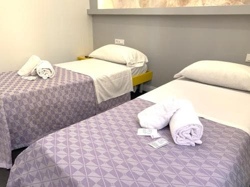 A cozy hotel room features two neatly made beds with purple patterned linens, white towels, and a calm ambiance, ideal for travelers seeking comfort and simplicity.