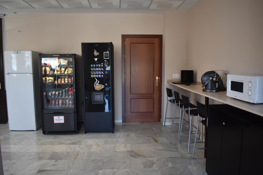 A cozy break room with marble flooring features vending machines, a coffee machine, and bar stools by a counter, ideal for travelers seeking a quick refreshment spot.