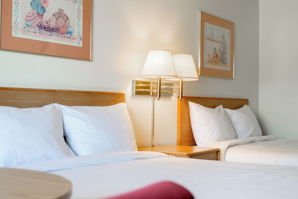 A cozy hotel room features two neatly made beds with wooden headboards, a warm-toned bedside lamp, and framed artwork, creating a serene atmosphere ideal for relaxation during a travel getaway.