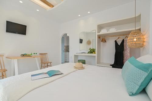 A cozy, modern bedroom with white walls, a neatly made bed adorned with turquoise pillows, a hanging wicker lamp, and a small dining area, evokes a serene and stylish retreat ideal for travelers seeking relaxation and comfort.