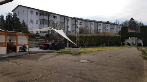A quiet residential courtyard features a paved area with a small outdoor seating space, surrounded by greenery and multi-story apartment buildings, ideal for travelers seeking a peaceful urban retreat.